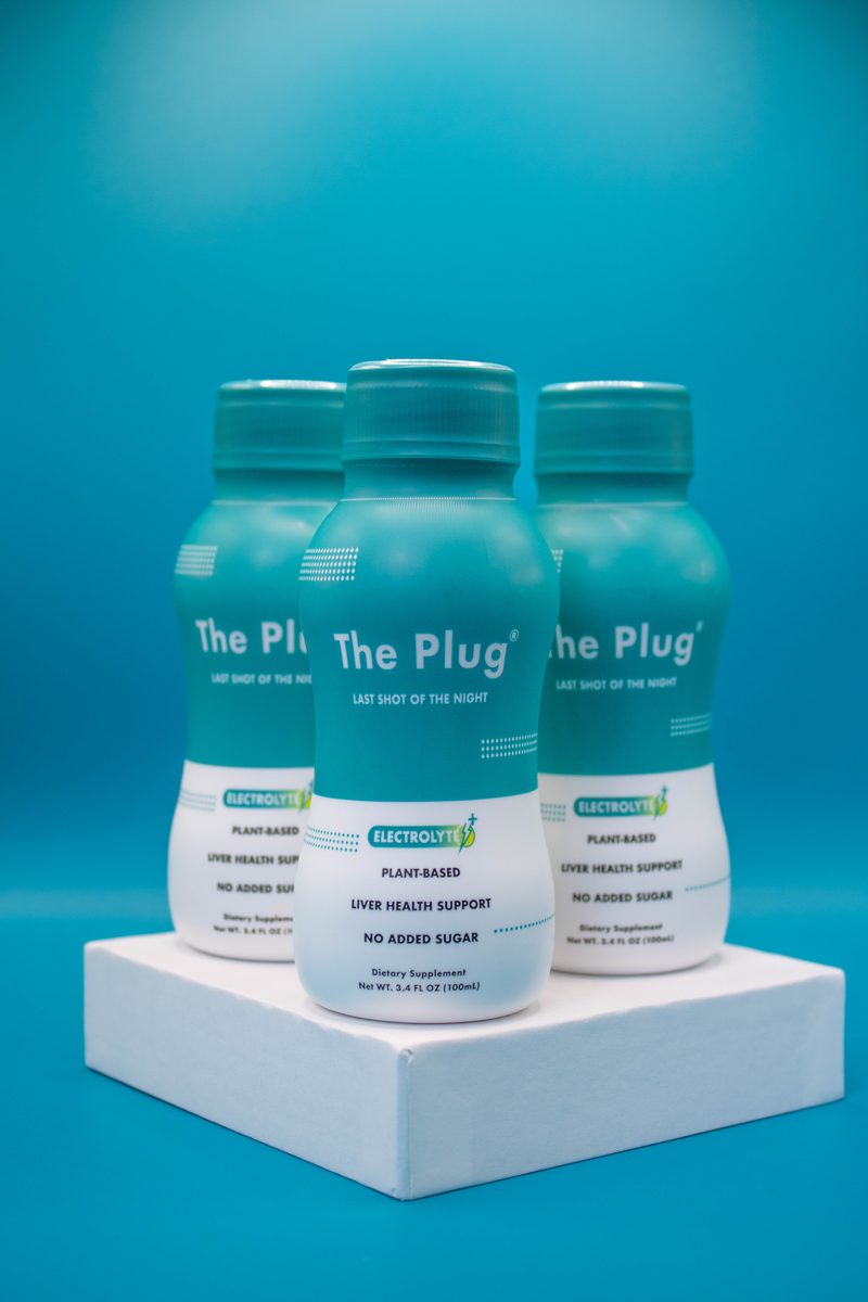 Three bottles of The Plug Drink on a teal studio set